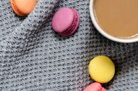 Background with gray plaid, coffee, cappuccino and multicolored appetizing macaroons, top view, flat lay. home comfort, warmth, care, tenderness.の写真素材