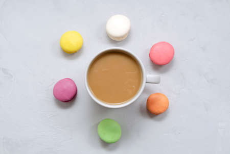 A cup of coffee with milk in the center and multi-colored macarons around it on a light concrete background with a place for text. Flat lay, top view.の写真素材
