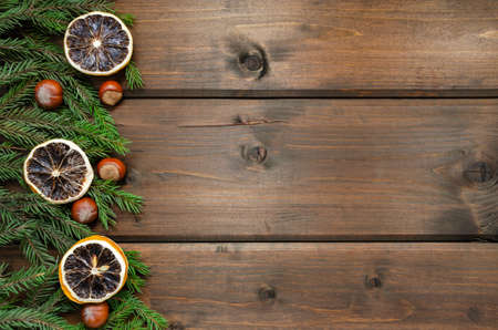 Dark brown vintage rustic wood background with Christmas decorations. Spruce branches, hazelnuts, dried lemon rings. Top view with copy space. layout for postcards, congratulations, billboardの写真素材