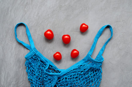 blue mesh eco-friendly shopping bag with zero waste with red cherry tomatoes in the shape of a...