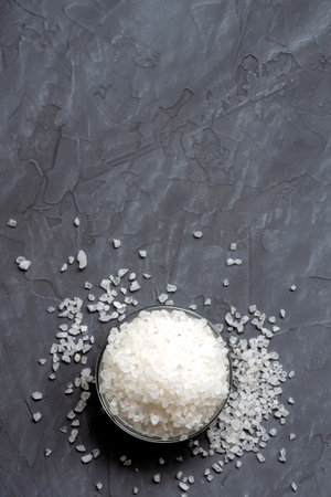 coarse white sea salt in a glass bowl is scattered on the table - top view. On a gray concrete background. copy spaceの写真素材
