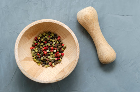 Multicolored red green black peppercorns in a wooden mortar with a pestle on a gray concrete background close-up with a place for text. seasoning. ingredients.の写真素材
