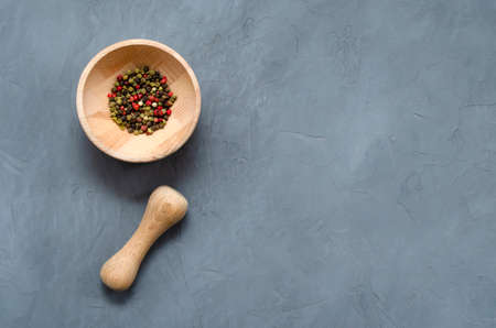 Multicolored red green black peppercorns in a wooden mortar with a pestle on a gray concrete background close-up with a place for text. seasoning. ingredients.の写真素材