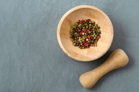 Multicolored red green black peppercorns in a wooden mortar with a pestle on a gray concrete background close-up with a place for text. seasoning. ingredients.の写真素材