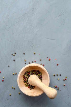 Multi-colored red green black peppercorns in a wooden mortar with pestle and scattered around on a ultimate gray concrete background close-up with a place for text. seasoning. ingredients.の写真素材