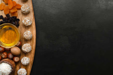 energy balls and ingredients for their preparation on a wooden board on a black slate background. nuts raisins coconut honey and dried apricots. recipe for a nutritious breakfast or snackの写真素材