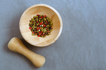 Multicolored red green black peppercorns in a wooden mortar with a pestle on a gray concrete background close-up with a place for text. seasoning. ingredients.の写真素材