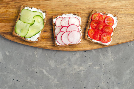 Vegetarian sandwiches with cream cheese, fresh cucumber, radish, tomatoes on a cutting wooden board on concrete. background. Flat lay. healthy food diet weight loss fitnessの写真素材