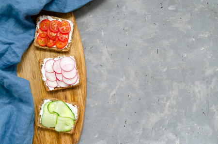 Vegetarian sandwiches with cream cheese, fresh cucumber, radish, tomatoes on a cutting wooden board...