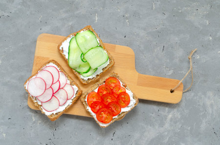 Vegetarian sandwiches with cream cheese, fresh cucumber, radish, tomatoes on a cutting wooden board on concrete. background. Flat lay. healthy food diet weight loss fitnessの写真素材