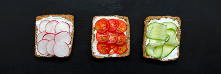 banner appetizing delicious vegetarian sandwiches with cream cheese, fresh cucumber, radish, tomato on black slate background. Flat layout. healthy food diet weight loss fitness. close-up.の写真素材