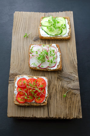 appetizing delicious vegetarian sandwiches with cream cheese fresh cucumber, radish, tomato and microgreens on black slate wood background. Flat layout. healthy food diet weight loss fitness. close-upの写真素材