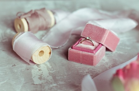 romantic present: pink velvet box with a wedding ring and light satin ribbons on a gray backgroundの写真素材