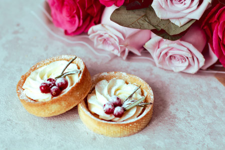 Tender romantic gift: sweet cakes with cream and berries and a bouquet of pink roses on a light