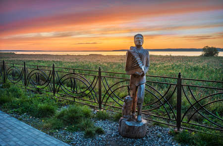 Beautiful pink sunset over Lake Galich in the Kostroma region and a wooden sculpture of a man with accordionのeditorial素材