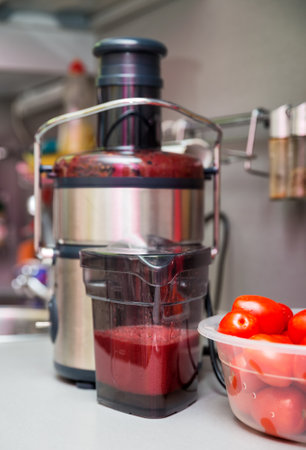 Squeezing tomato juice at home. Juicer in the kitchen. Focus on the foregroundの写真素材