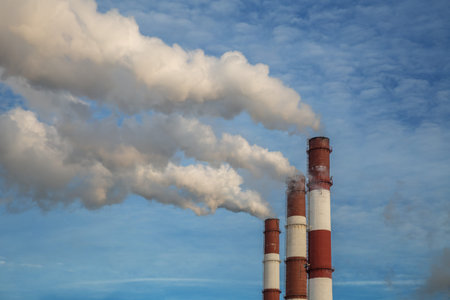 Factory chimney and white smokes and steam against a blue sky background