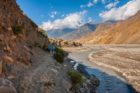 Trekking in the Himalayas. Tourists with backpacks on trail along banks of the Kali Gandaki River amid picturesque Himalayan landscape, Lower Mustang, Nepal.の写真素材