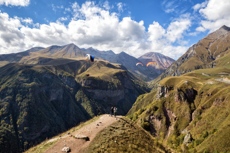Scenic mountain landscape. Two women tourists take pictures as paragliders fly over gorge, the...