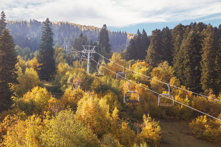 Ski resort in fall. Empty chairlift above trees with yellow foliage. Sunny autumn mountain landscape. Georgia, Svanetiの写真素材