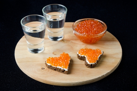 two sandwich with red caviar in the form of a heart and vodka on a wooden boardの写真素材