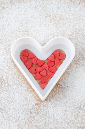 Sugar hearts in white baking dish on a board sprinkled with powdered sugar on a wooden boardの写真素材