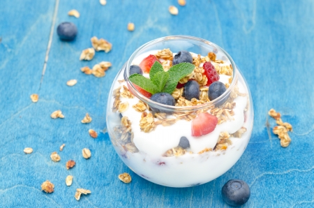 layered dessert with yogurt, granola, fresh berries garnished with mint on a blue background horizontalの写真素材