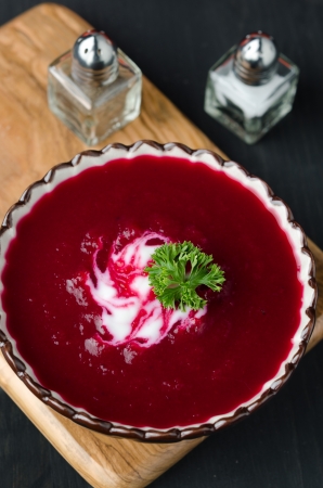 A bowl of tomato soup with beetroot, yoghurt and decorated with greens on a wooden board, top viewの写真素材