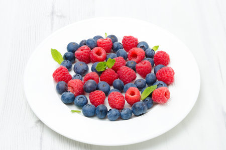Fresh raspberries and blueberries on the plate on a white table