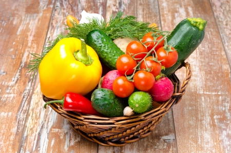 assorted fresh vegetables and herbs in a wicker basket on a wooden background close-upの写真素材