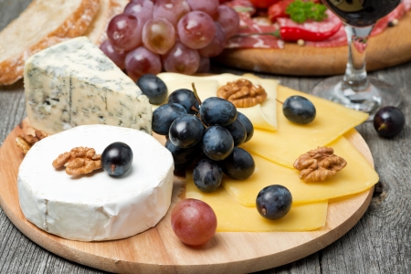 Assorted cheese, grapes, wine and sausages on wooden boardの写真素材