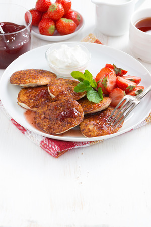 Pancakes with fresh strawberries, jam and tea. White wooden background for text, vertical, top view Pancakes with fresh strawberries, jam and tea. White wooden background for text, vertical, top view