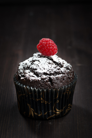 chocolate muffins with powdered sugar and raspberry on a dark background, verticalの写真素材