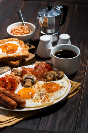 Fried eggs with bacon, sausages and vegetables for breakfast on wooden table, vertical, closeupの写真素材