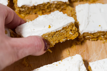 Hand holding carrot cake with icing, closeup