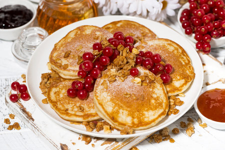 tasty pancakes with berries and honey on a white wooden table, closeup