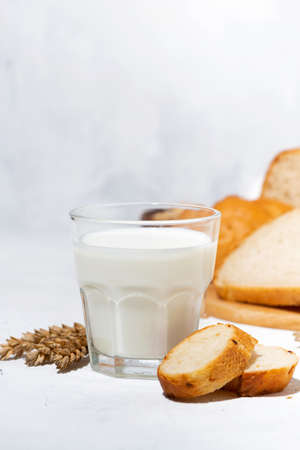 glass of milk, assortment of fresh bread on white table, verticalの写真素材