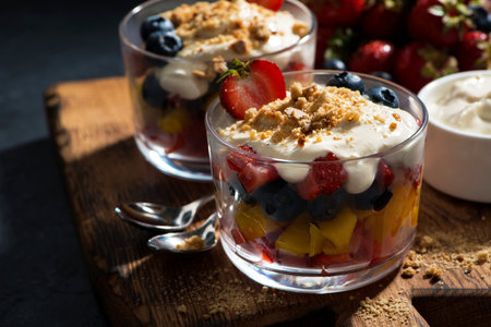Assorted fresh fruit with custard in glasses on a wooden board, horizontal, closeupの写真素材