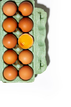 package of fresh whole chicken eggs and one broken egg on white background, vertical top viewの写真素材