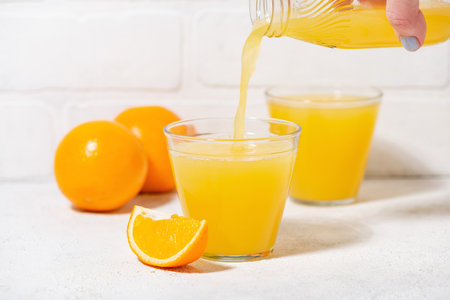 man pouring freshly squeezed orange juice into a glass, horizontal photo closeupの写真素材