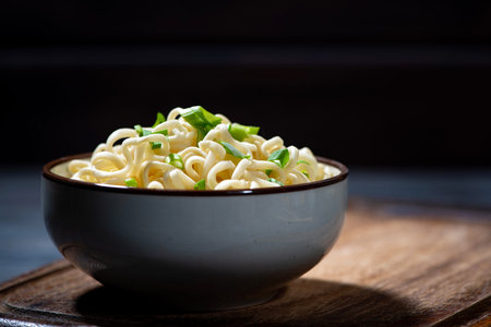 bowl of hot egg noodles with vegetables on dark background, horizontal closeup