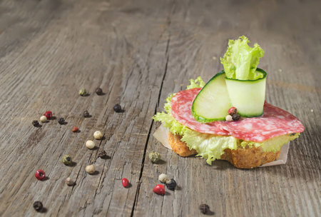 Sandwich with salami sausage, cucumber and salad on wooden backgroundの写真素材