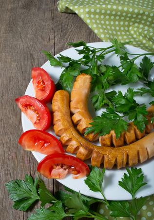 Grilled sausages with tomato and parsley on a wooden tableの写真素材