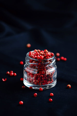 Pink pepper spice in glass jar on dark background