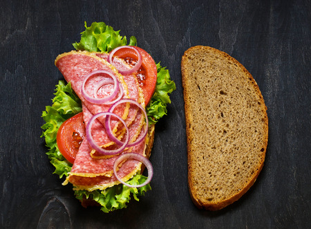 Sandwich with tomato, salami, salad, onion on dark background. Selective focusの写真素材