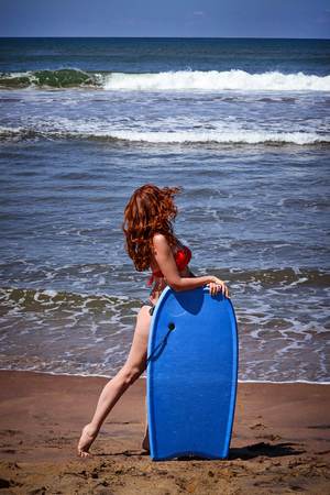 Red-haired girl with surfboard on the beachの写真素材