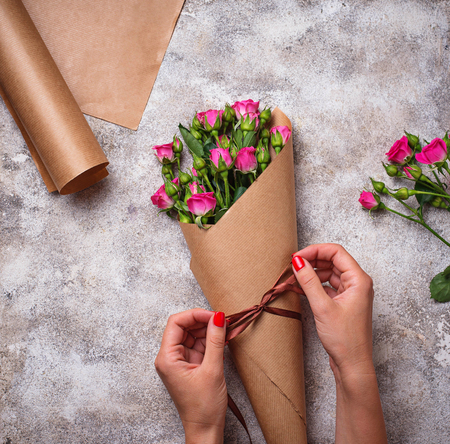 Womens hands wrap a bouquet of roses in paperの写真素材
