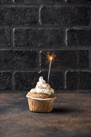 Birthday cupcake with cream and sparkler on brick wall backgroundの写真素材