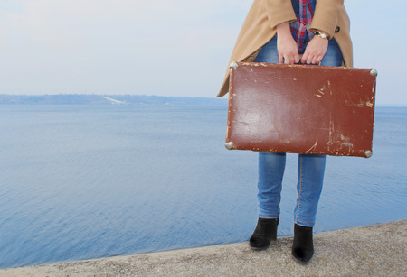 Girl\'s hands holding a vintage suitcase standing near the seashoreの写真素材