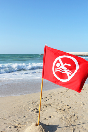 "No swim" sign on a sandy beach in a storm. Sunny and windy weather at seaの写真素材